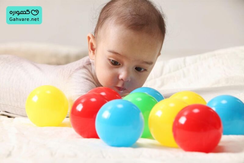 نوزادی در حال بازی با توپ های رنگی